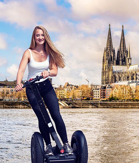 Fröhliche junge Frau genießt eine Segway Tour Köln am Rhein, mit dem majestätischen Kölner Dom im Hintergrund